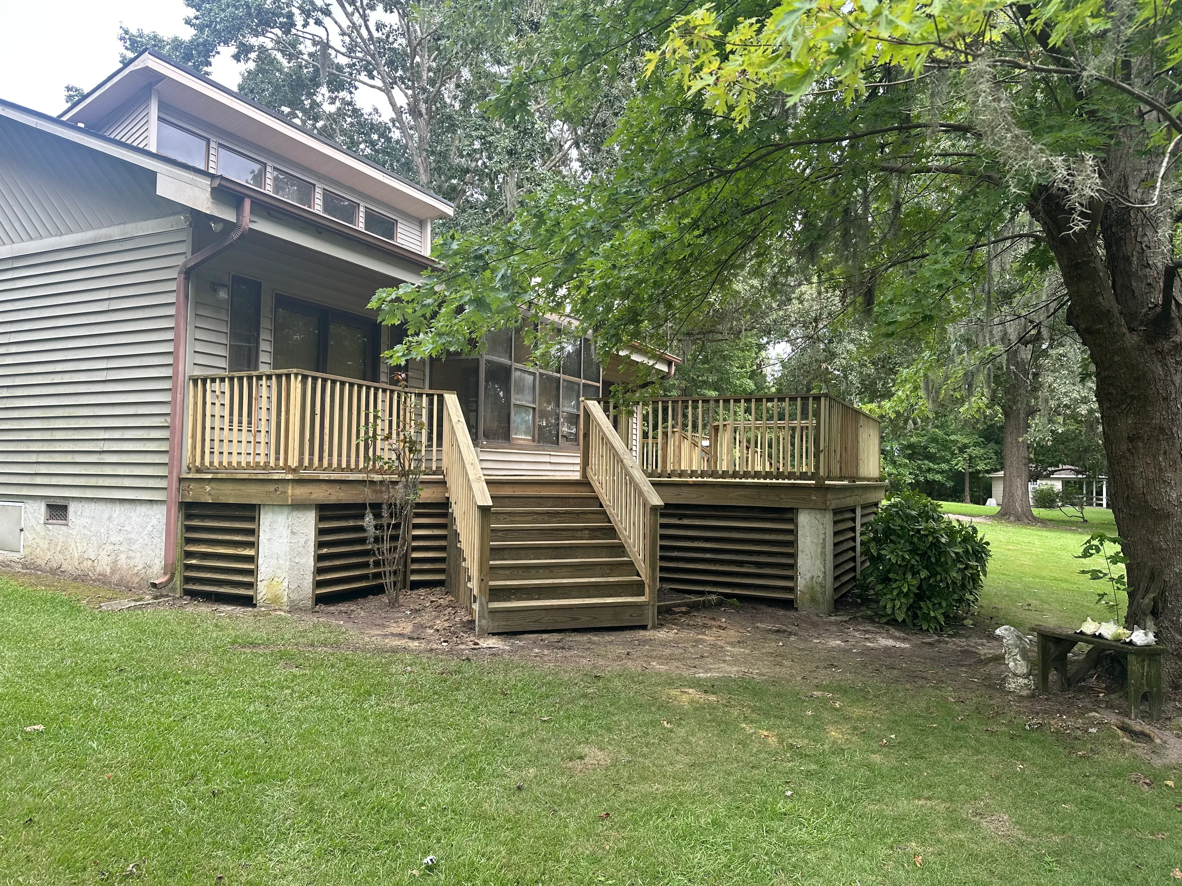 Multi-level wood deck with vertical railings, covered porch, and central stairs on residential home