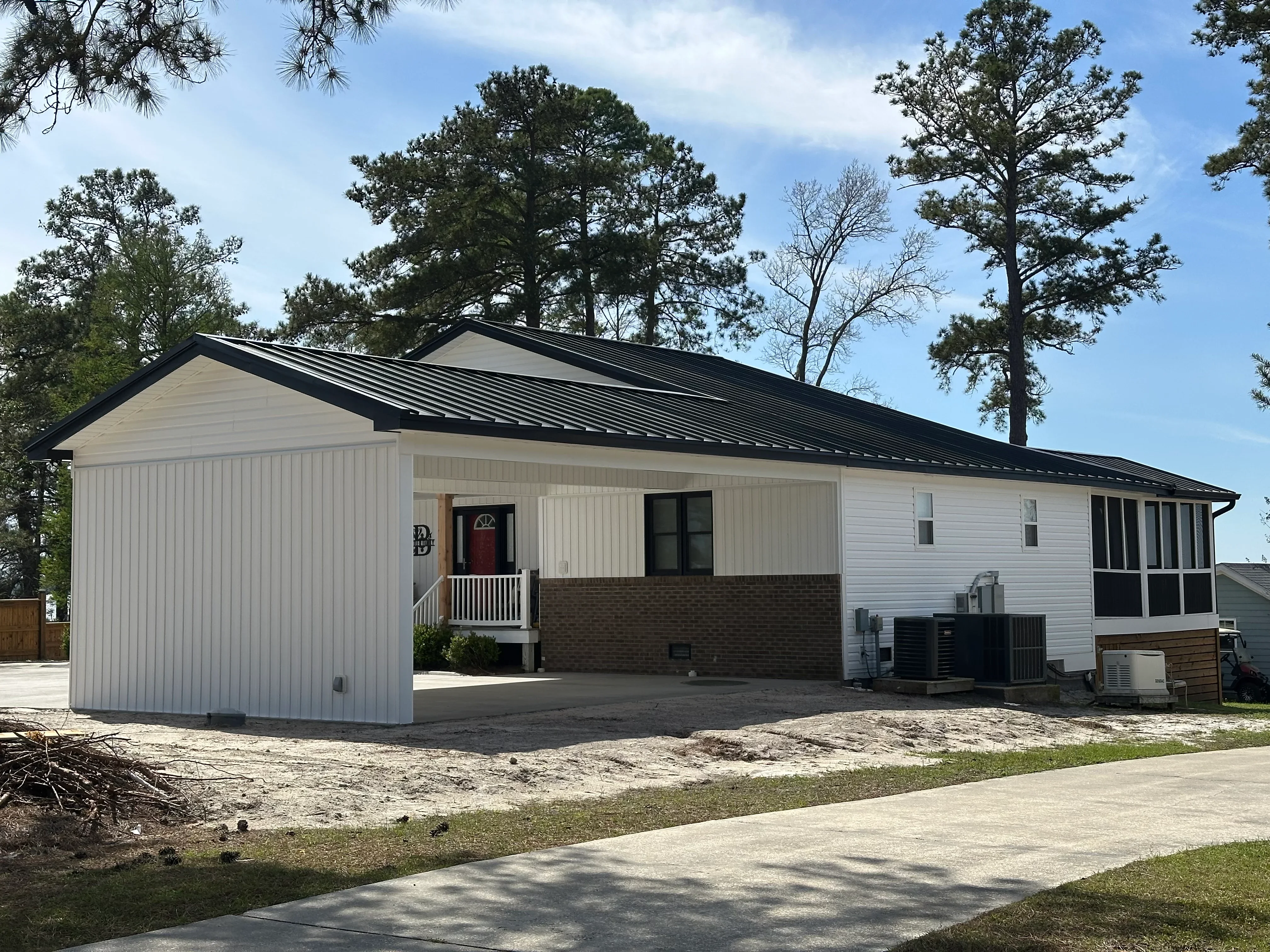 Black standing seam metal roof with white metal siding and brick veneer on residential home