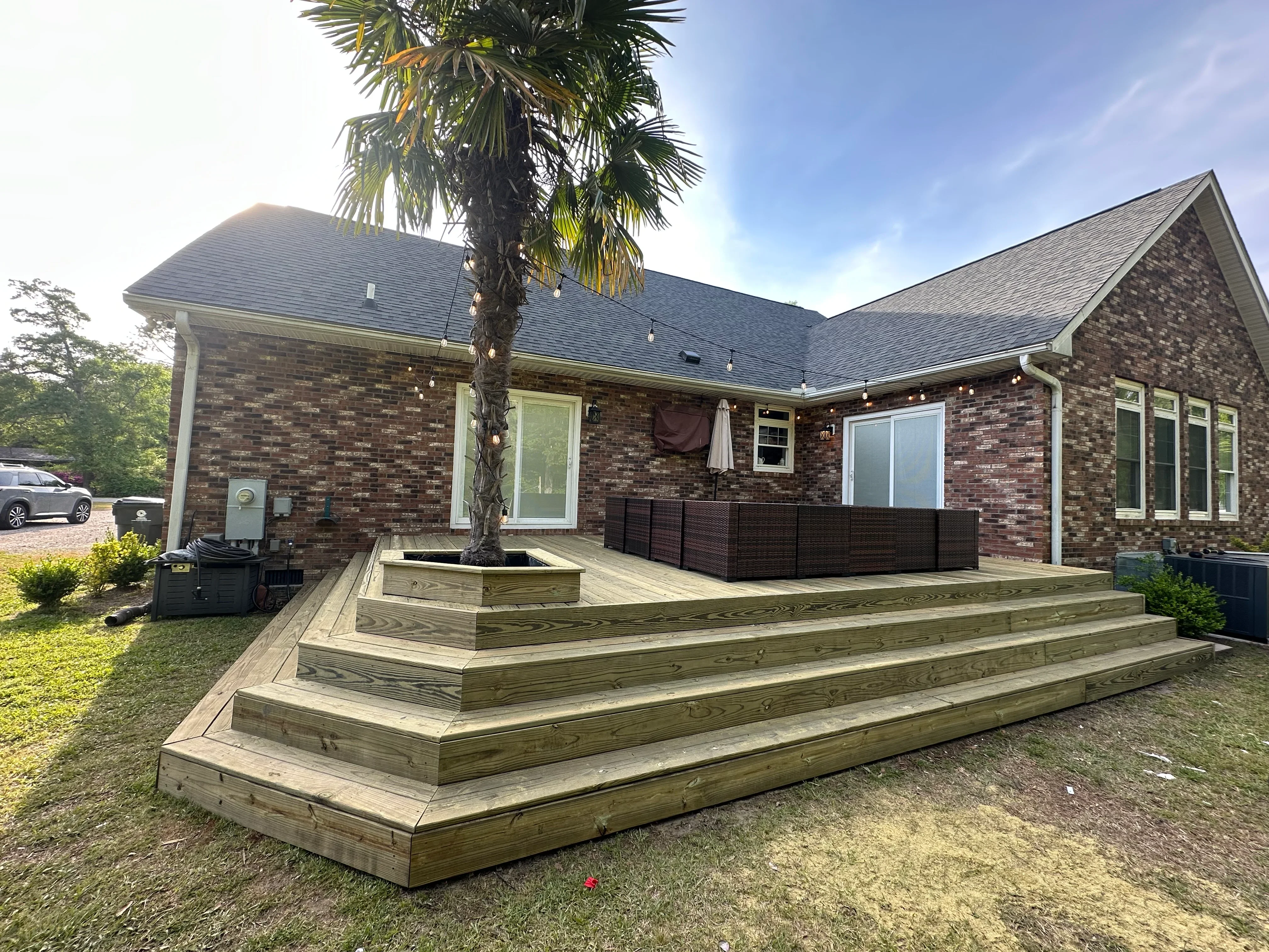 Multi-level pressure-treated wood deck with integrated planter box and palm tree, brick home backdrop