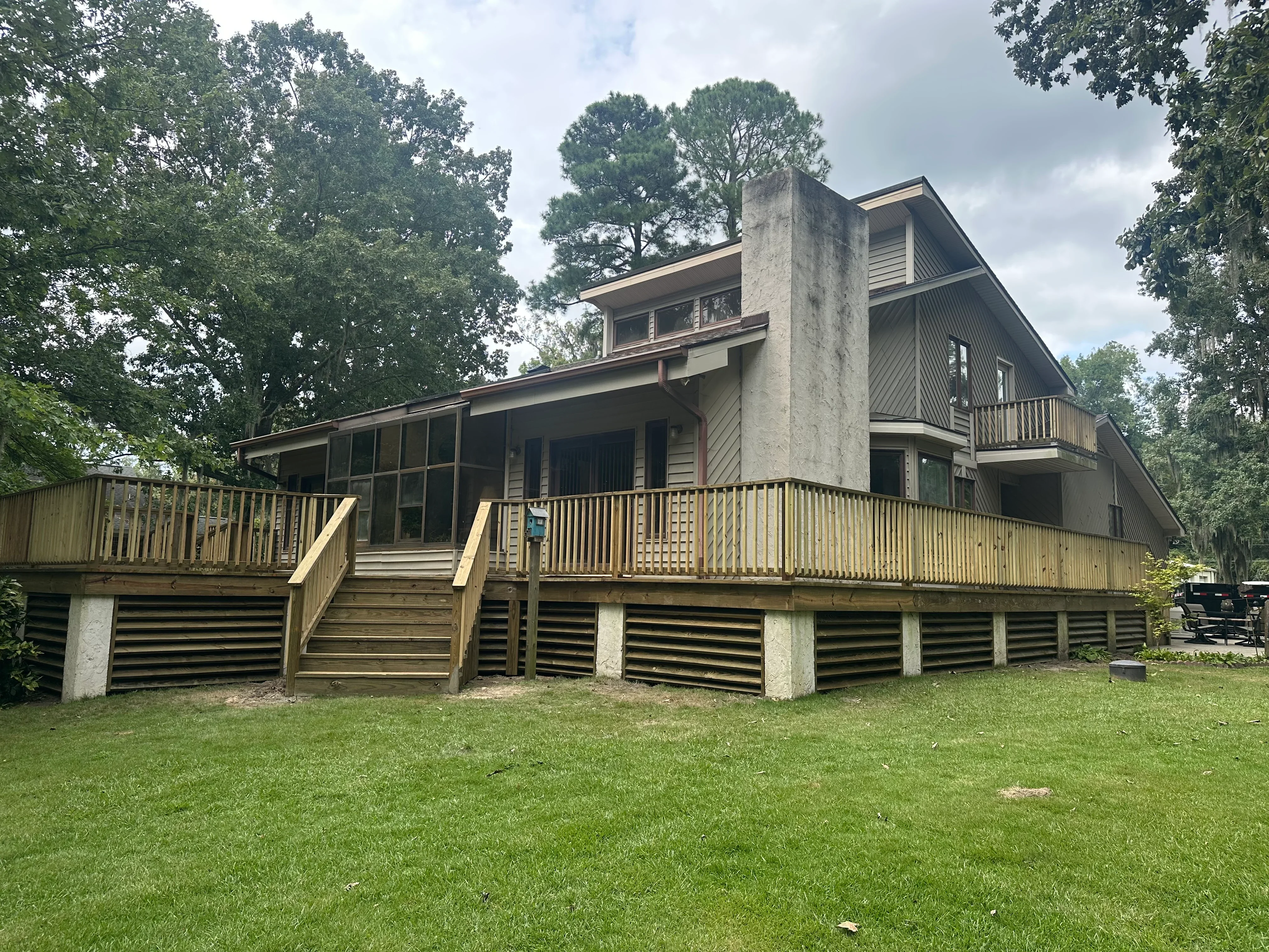 Modern elevated home with composite roof, concrete pillars, wooden deck railings, and mixed siding materials