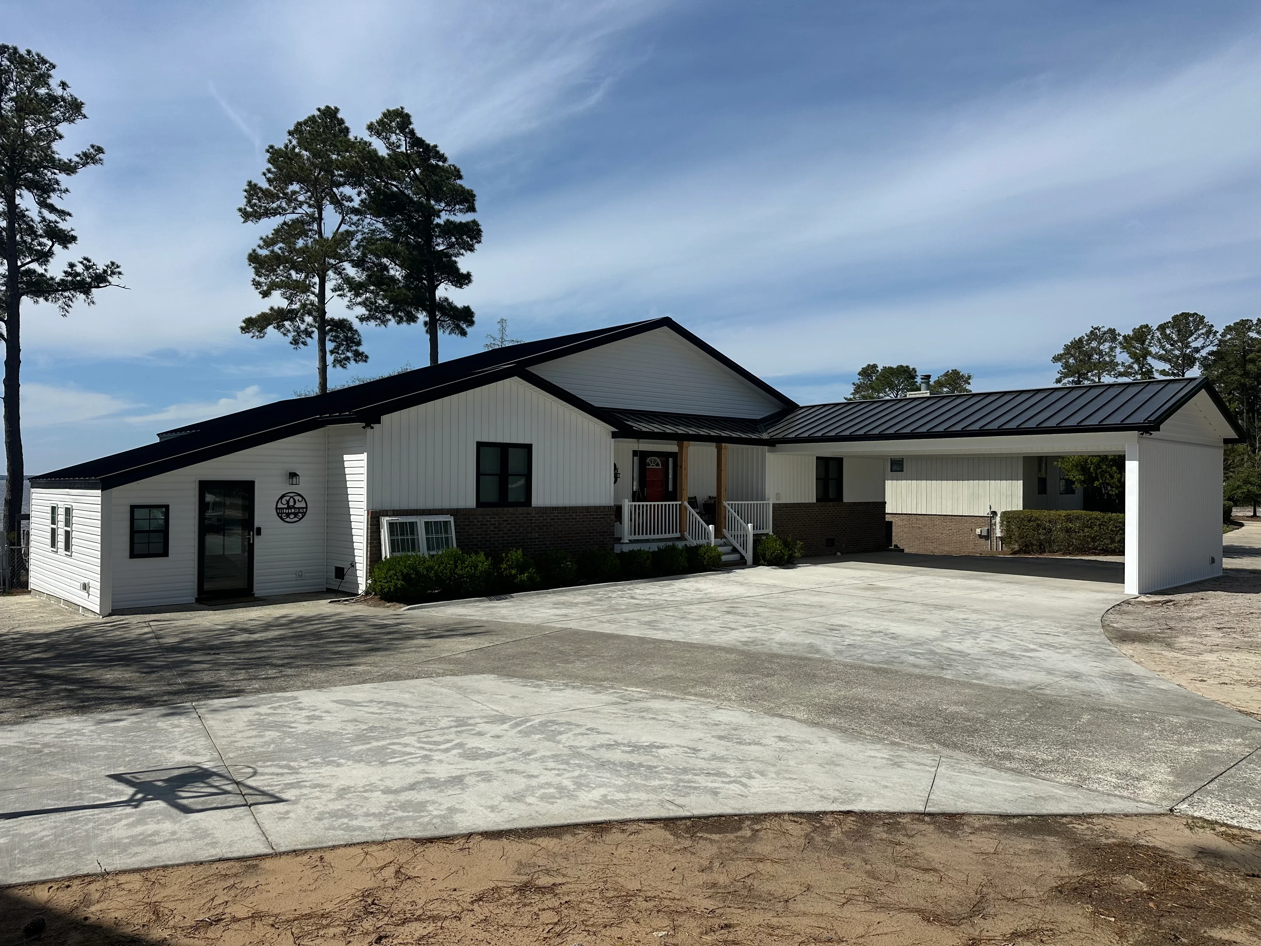 Black standing seam metal roof on white residential home with brick base and concrete driveway