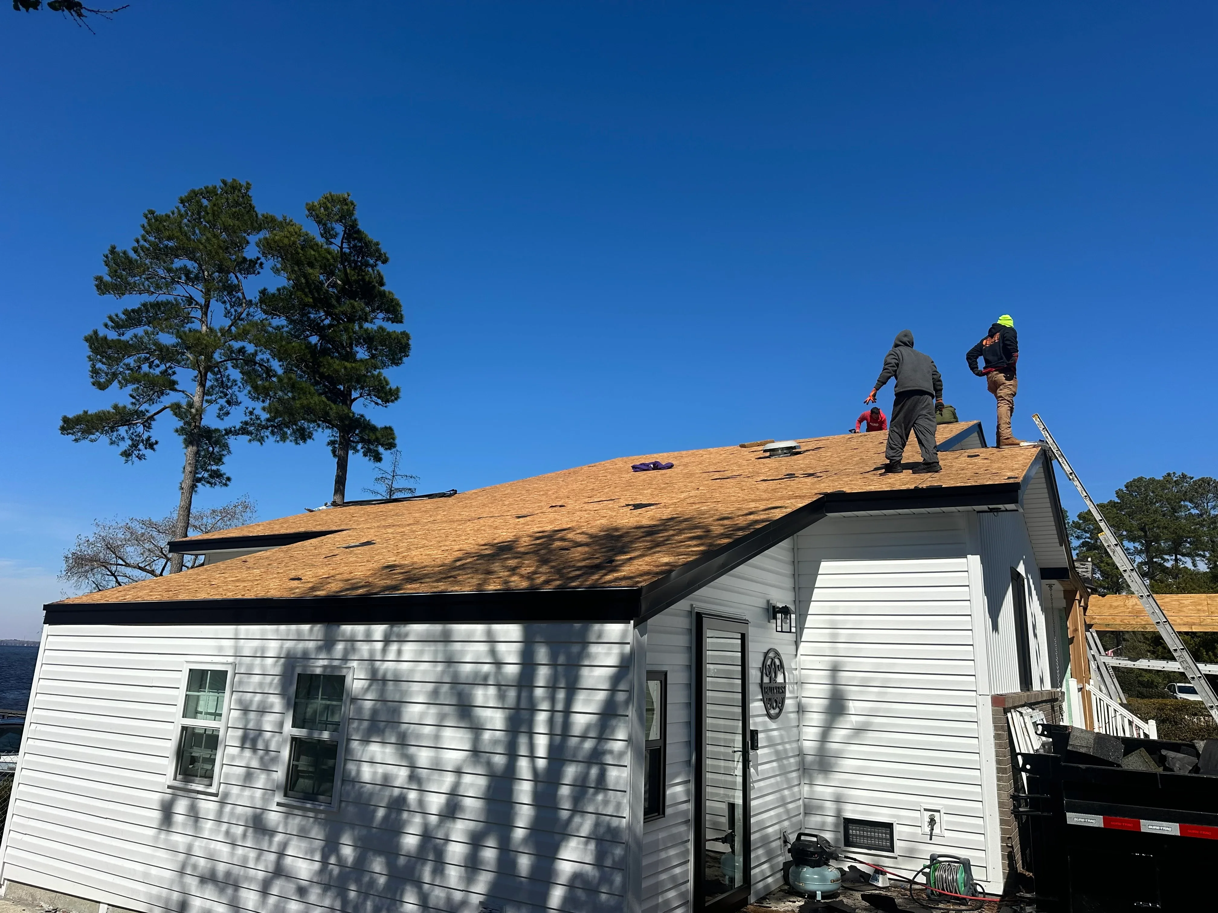 New tan architectural shingles installed on residential roof with workers on site